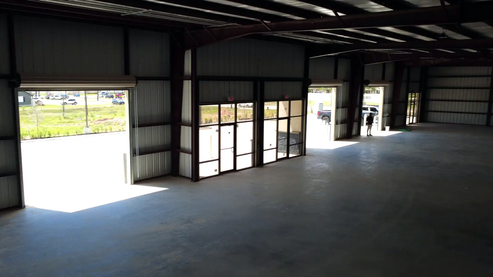 Inside a space: glass storefront doors and an open roll-up door, looking out to the lot